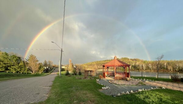 Double rainbow over gazebo and river landscape.