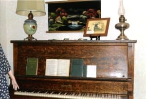 Antique upright piano with books and lamps on top.