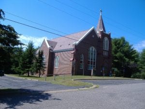 Brick church building with tall steeple and large windows.