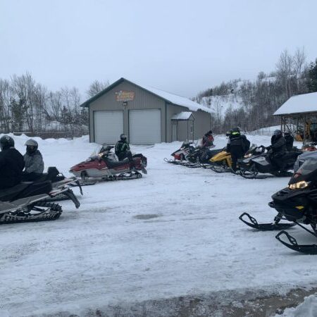Riders preparing snowmobiles near winter storage barn.