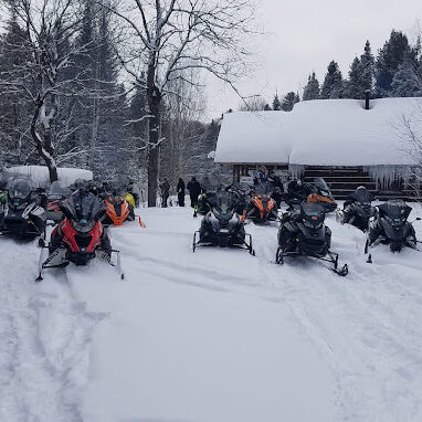 Snowmobiles parked outside a snowy cabin in the woods.